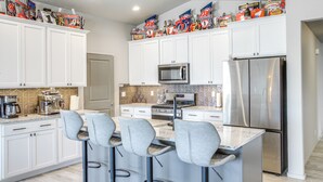 A modern kitchen with white cabinets, a stainless steel refrigerator, a microwave, and a bar area with stools. - 3 Mi to Spokane River! Furnished Patio & Yard (Post Falls)