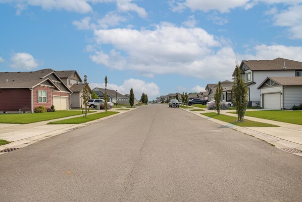 A residential street with houses on both sides, a clear sky, and a few parked cars. - 3 Mi to Spokane River! Furnished Patio & Yard (Post Falls)