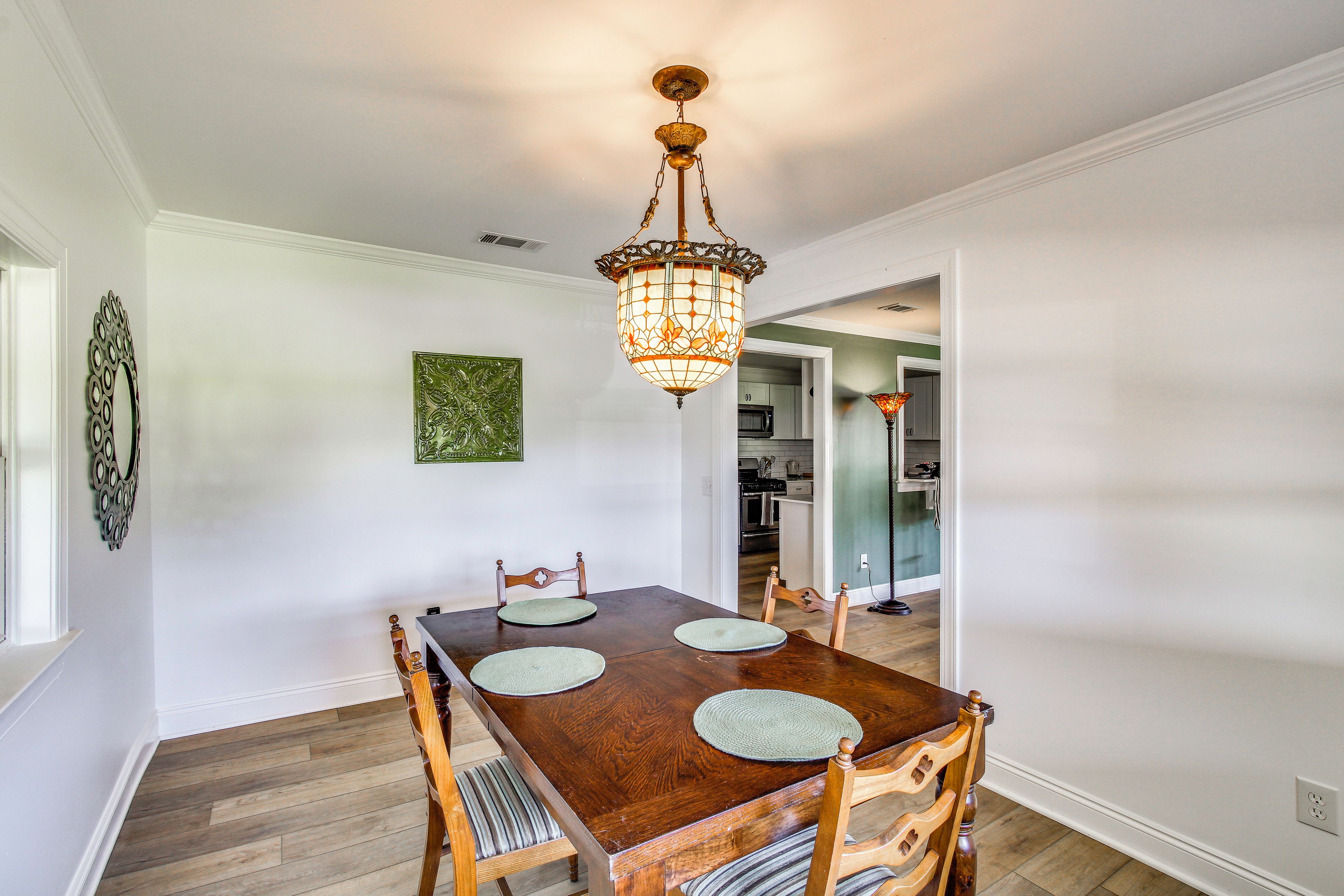 A dining area with a wooden table and chairs, a chandelier, and a kitchen in the background.