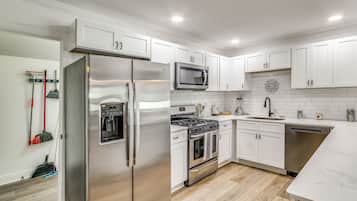 A modern kitchen with stainless steel appliances, white cabinetry, and a wooden floor.