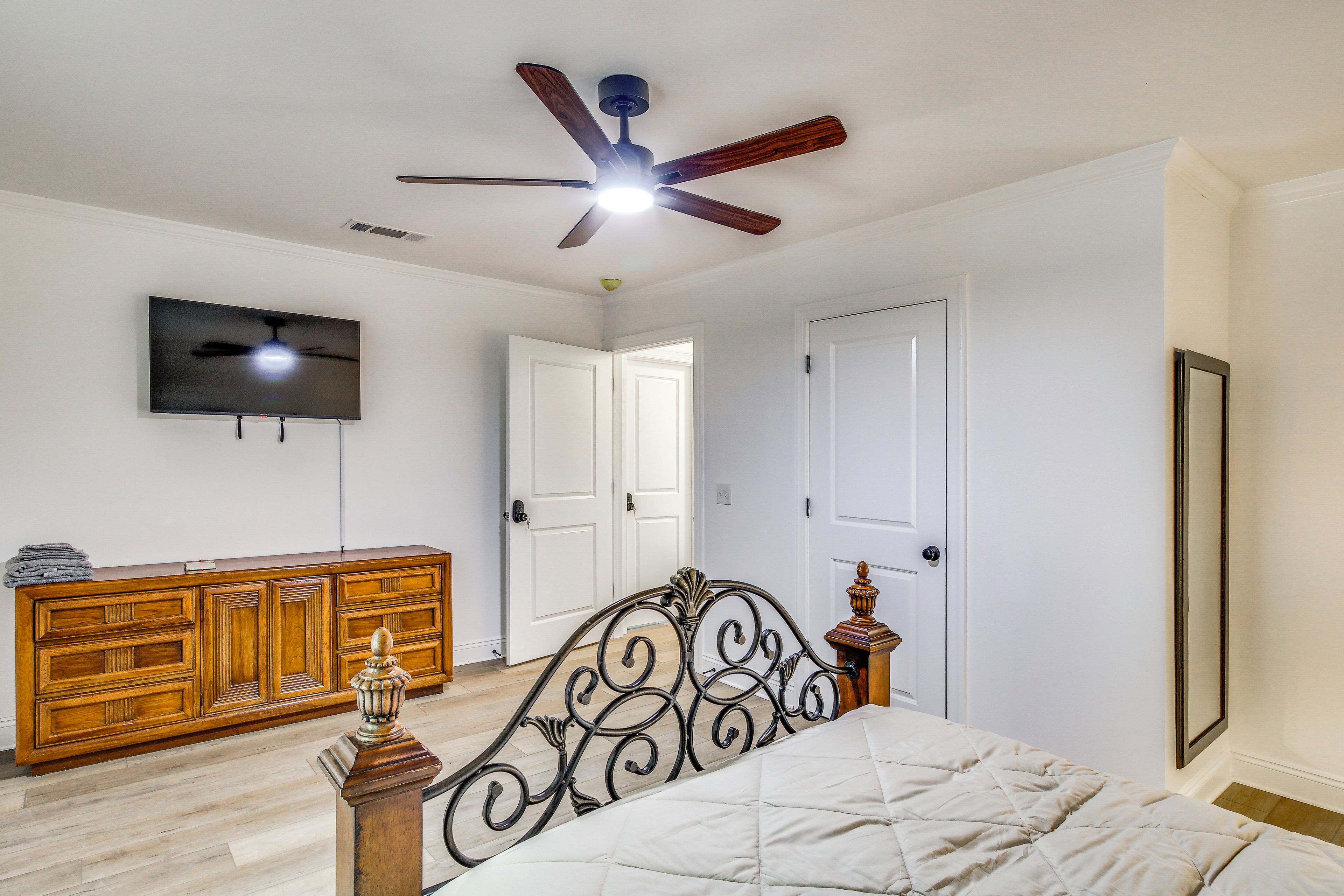 A bedroom with a bed, a wooden dresser, a television, and a ceiling fan.