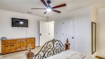 A bedroom with a bed, a wooden dresser, a television, and a ceiling fan.
