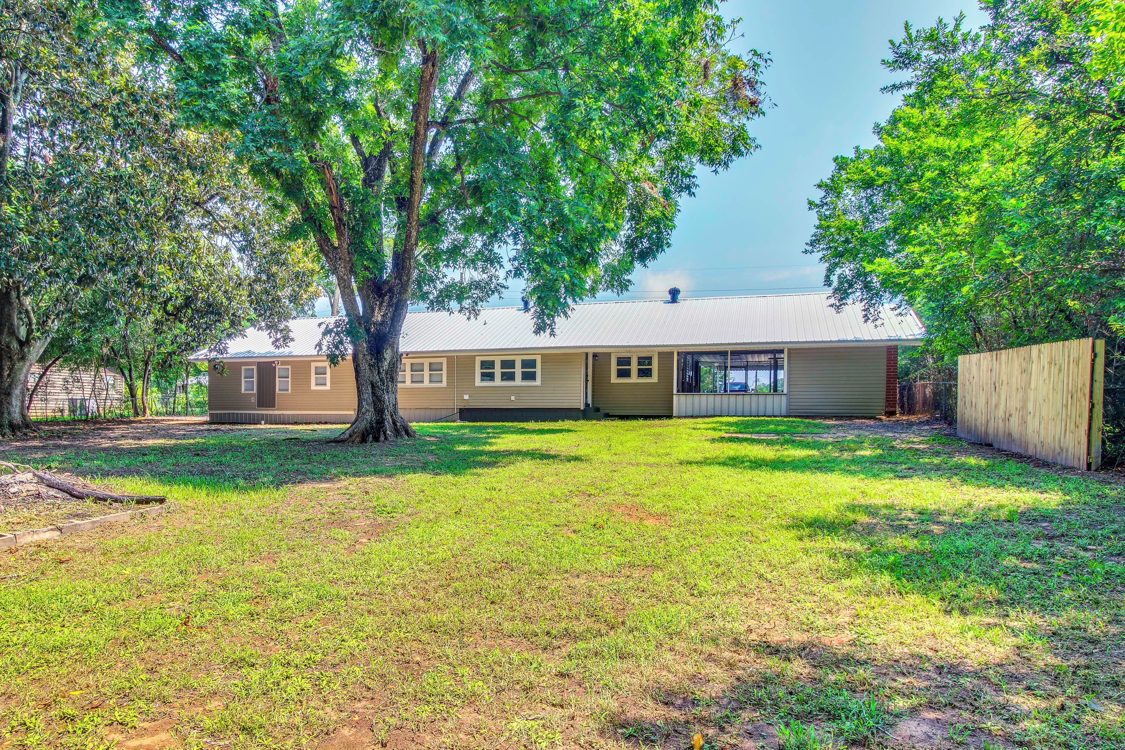 A residential property with a single-story house, a fenced yard, and mature trees.