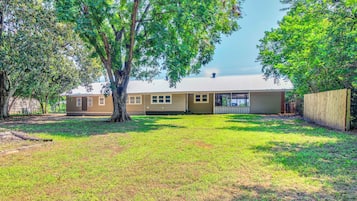 A residential property with a single-story house, a fenced yard, and mature trees.