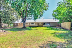 A residential property with a single-story house, a fenced yard, and mature trees.