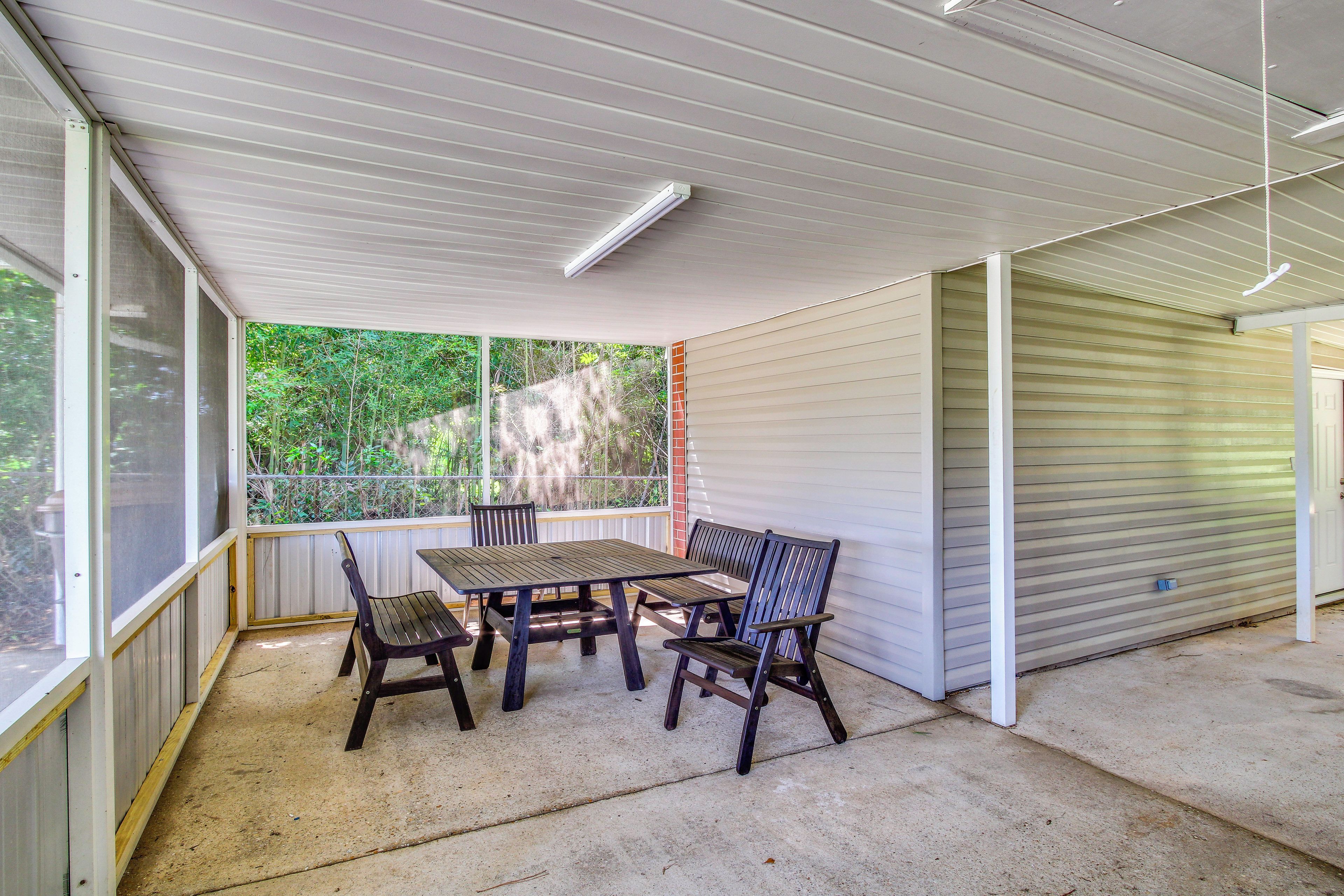 A covered patio area with a table and chairs, a view of greenery outside, and a closed garage door.
