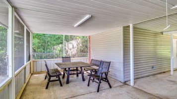 A covered patio area with a table and chairs, a view of greenery outside, and a closed garage door.