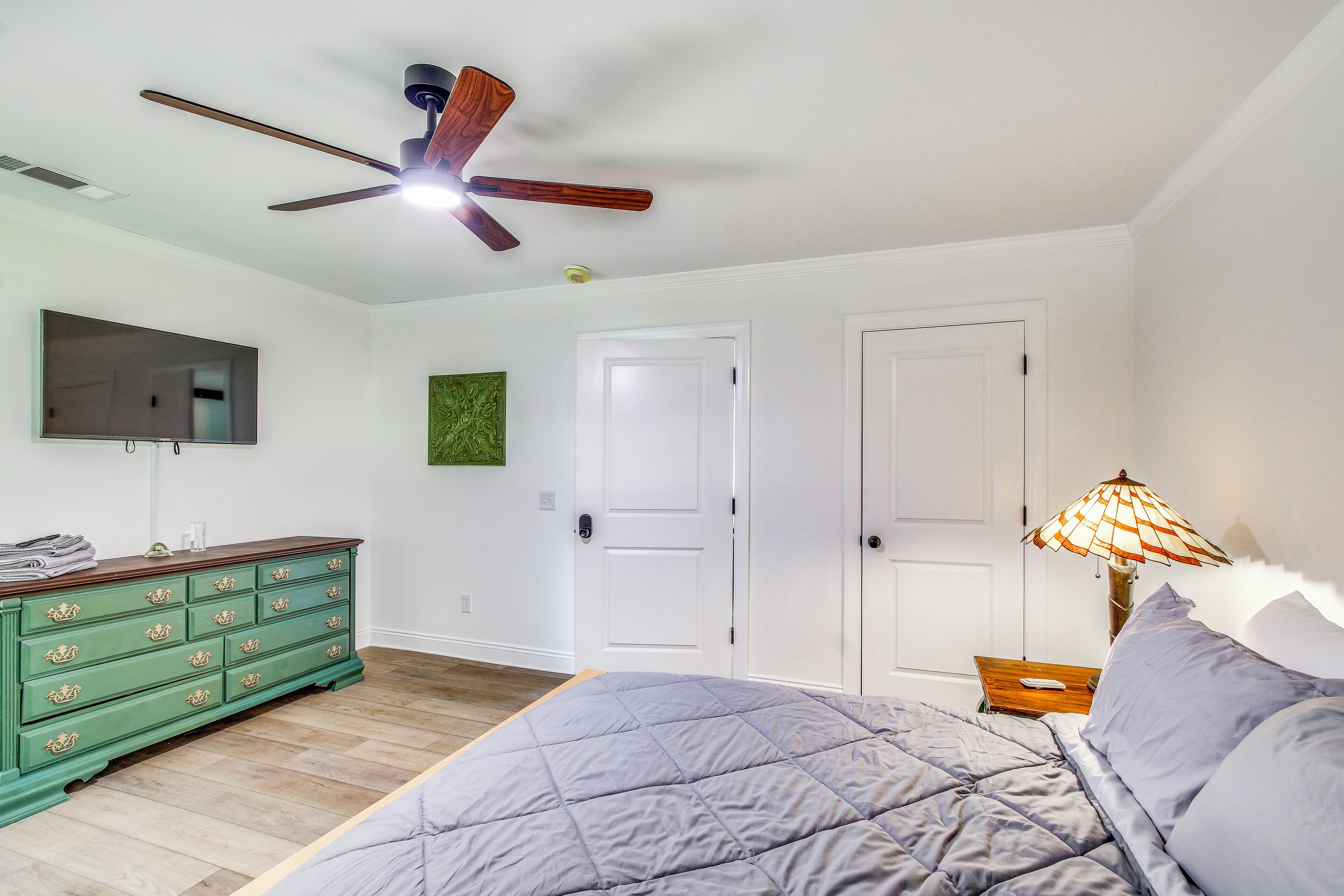 A bedroom with a bed, dresser, television, and a ceiling fan.