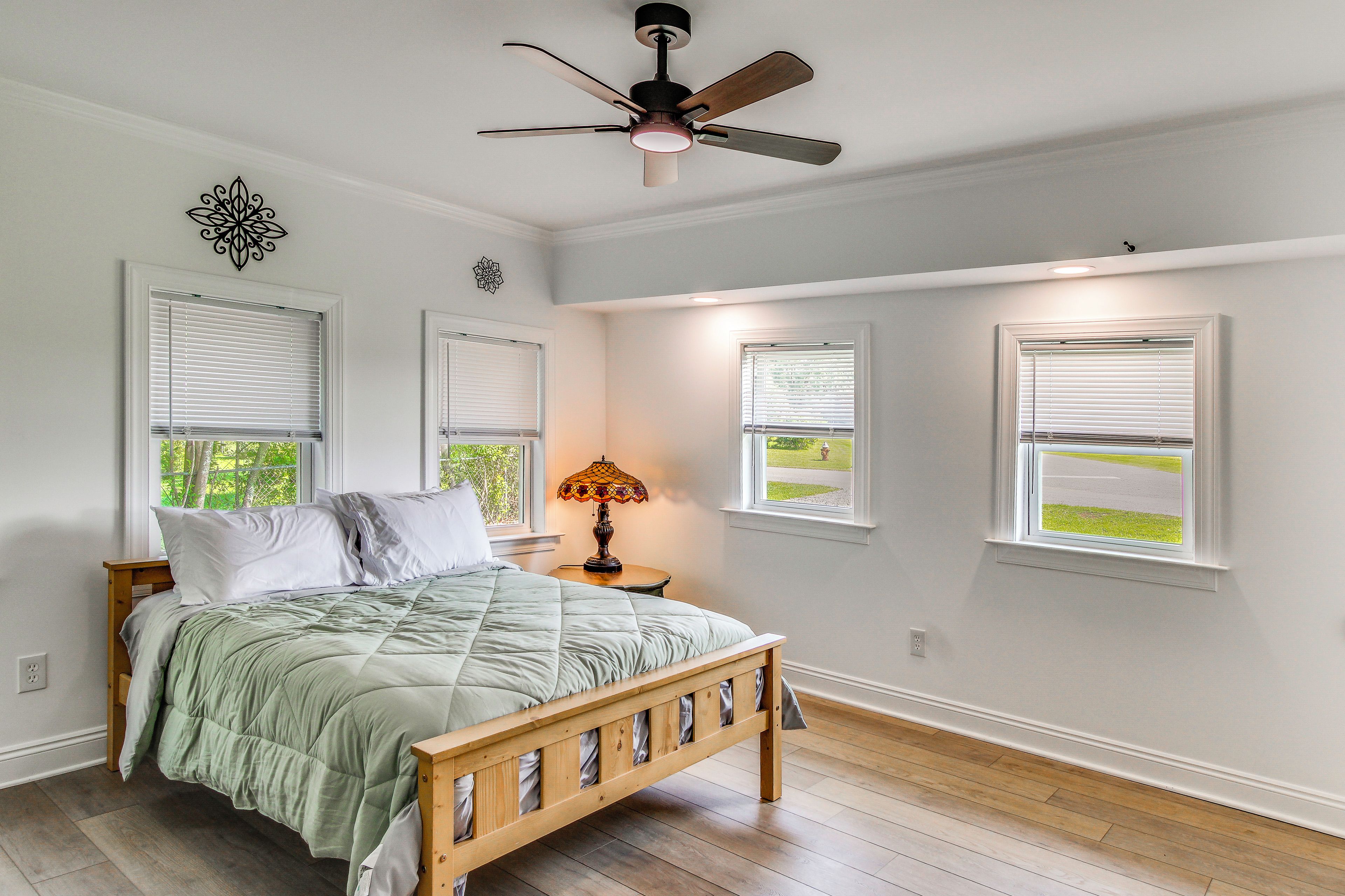 Un dormitorio con cama, ventilador de techo y tres ventanas.