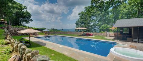 Una piscina con detalles de piedra, un jacuzzi y mobiliario exterior con sombrillas.