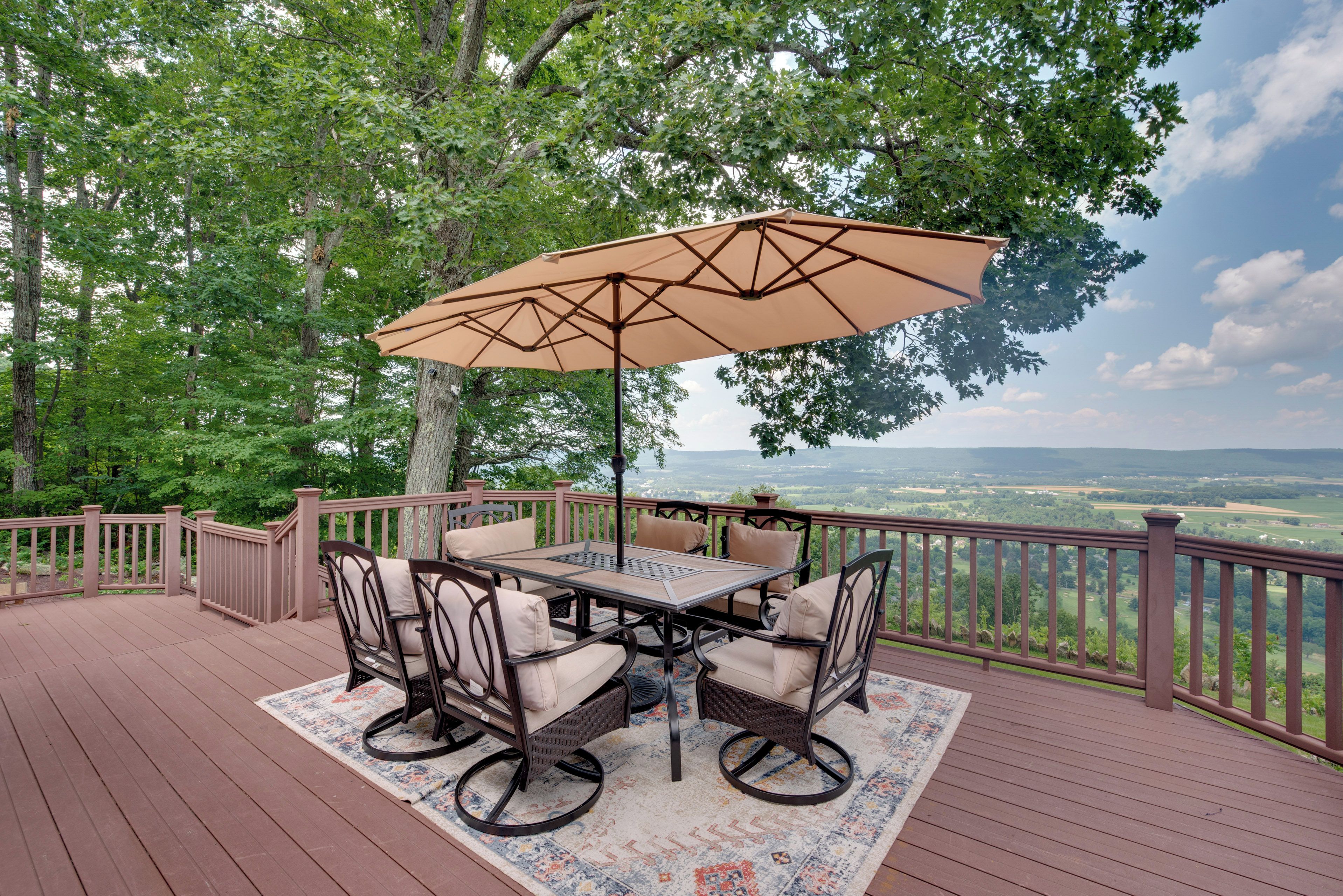 A deck with a table and chairs, a large umbrella, and a view of the landscape.
