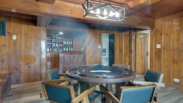 A wooden interior with a round table and chairs, a bar area with bottles, and a ceiling light fixture.