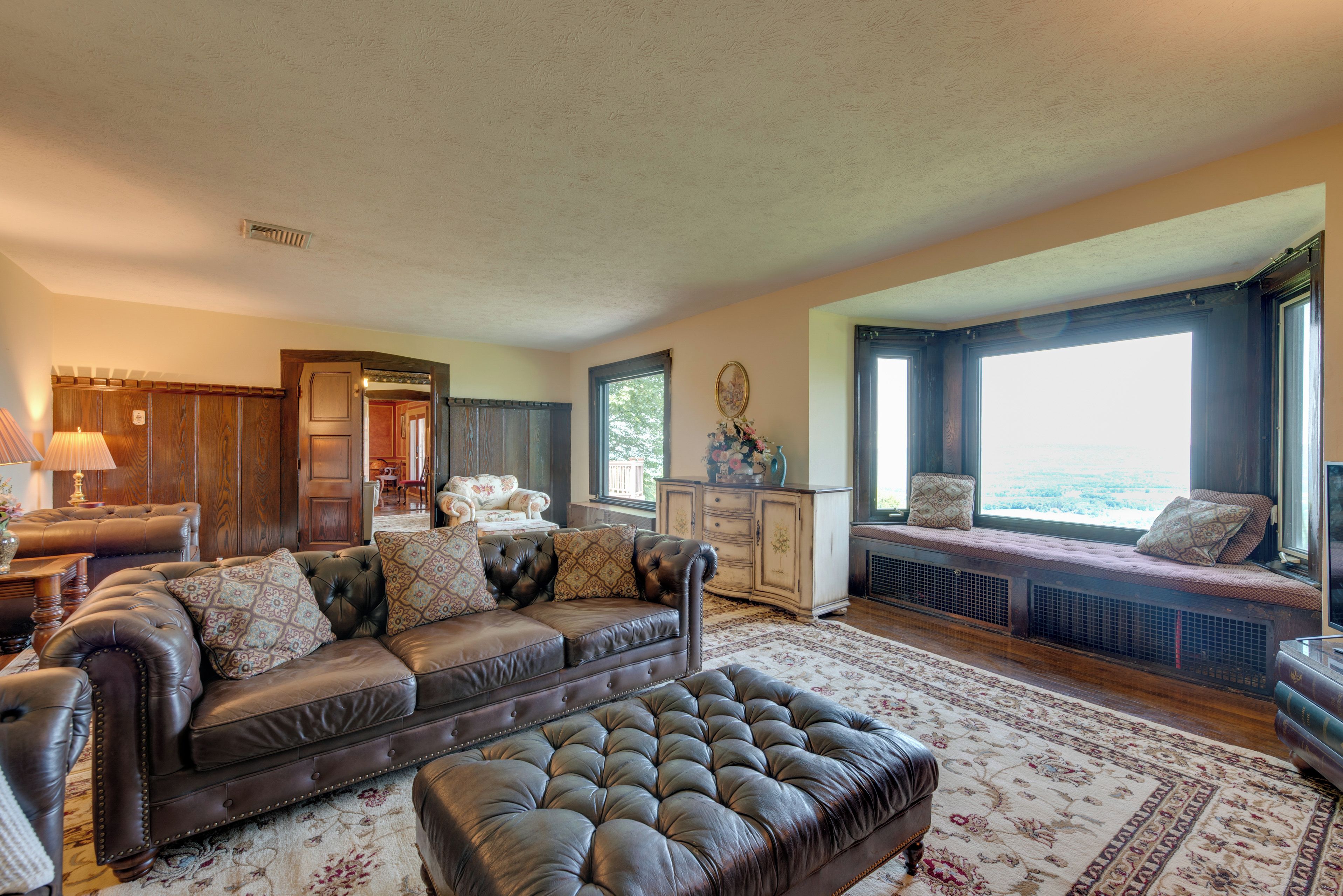 A spacious living room with a leather sofa, a large ottoman, and a view of the outdoors through a window.