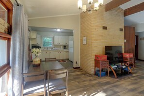 A dining area with a wooden table and chairs, a vase with flowers, and a kitchen in the background.