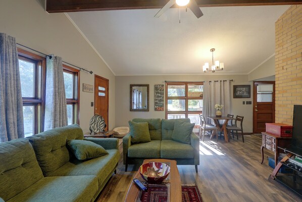 A living room with green sofas, a coffee table, and a dining area with a table and chairs.