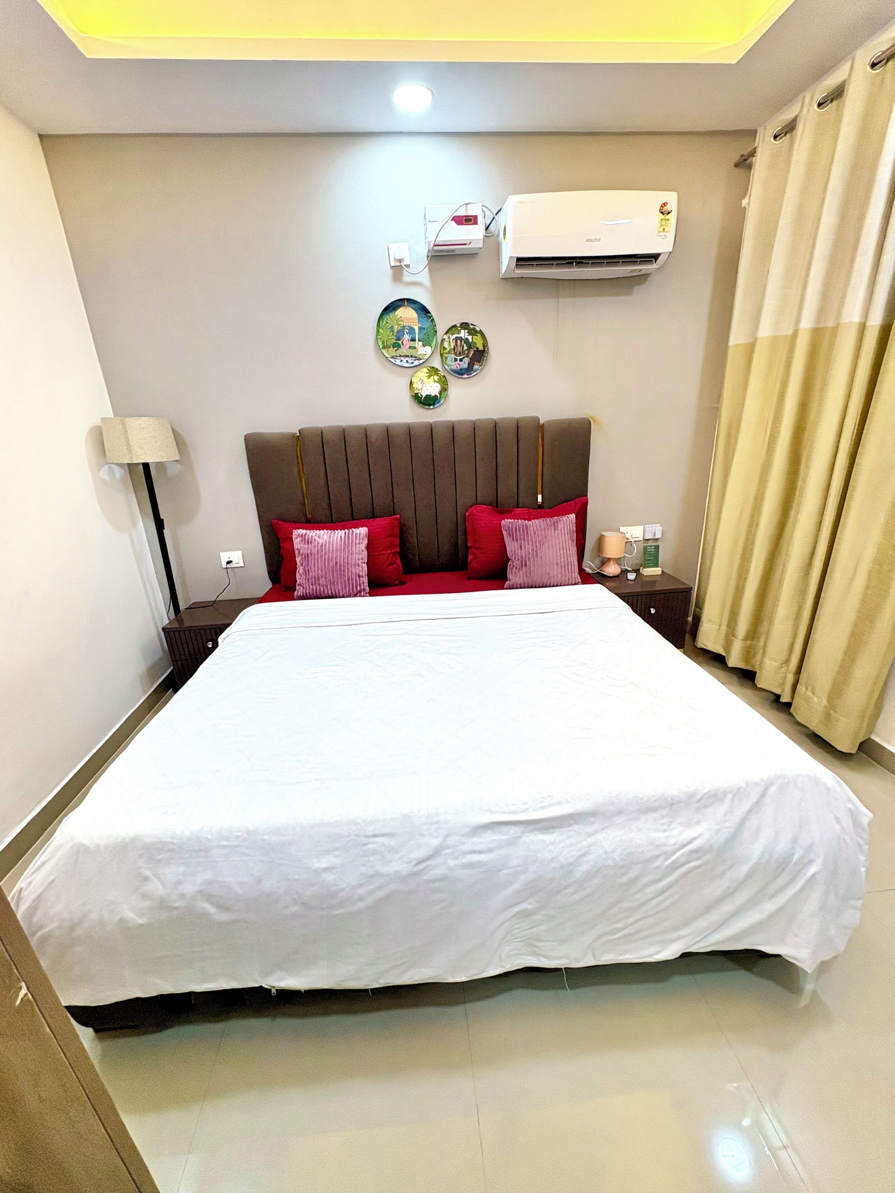 Habitación de hotel con una cama grande, aire acondicionado de pared y una mesita de noche con una lámpara y una taza.
