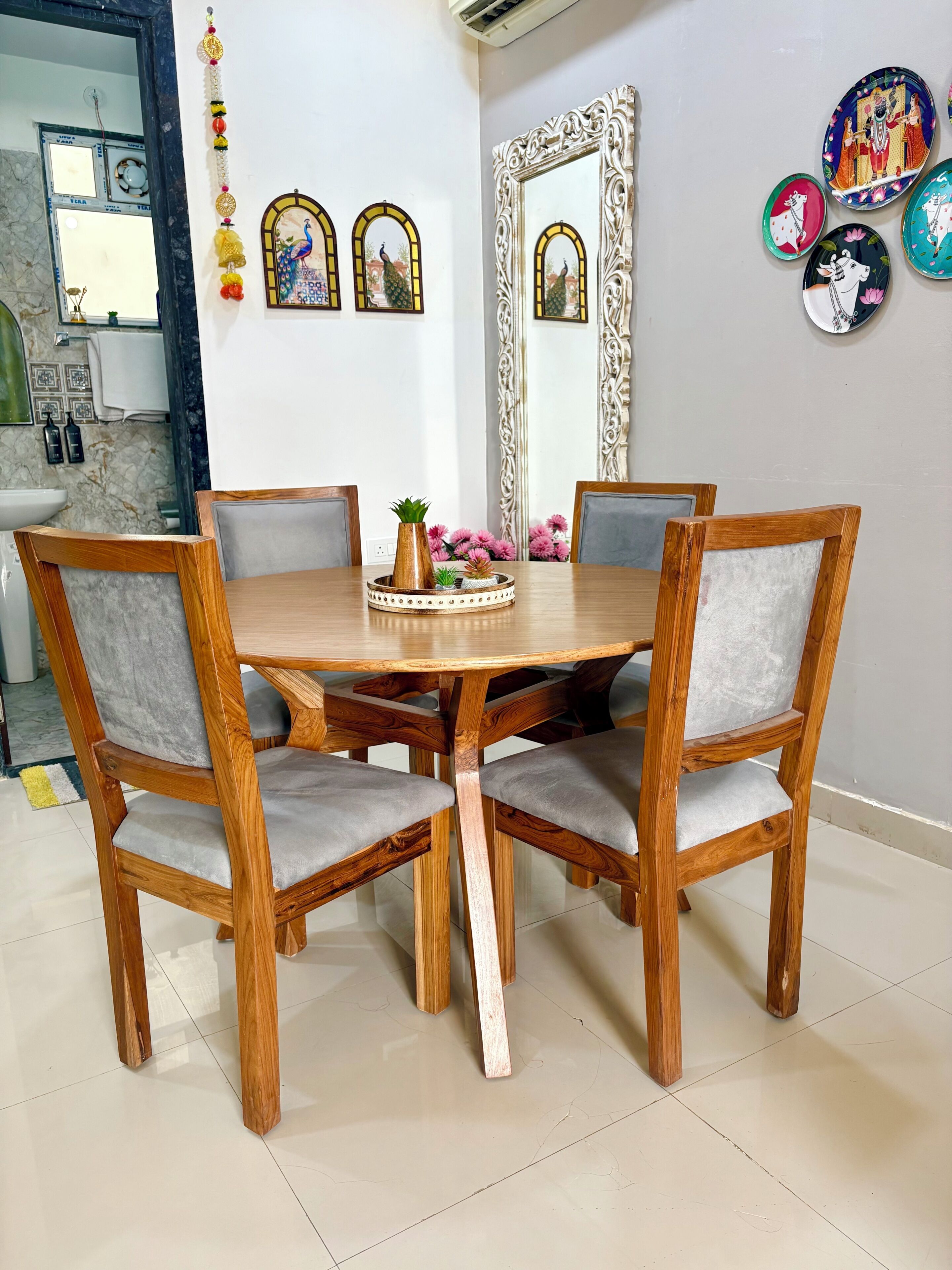 Un comedor con una mesa redonda de madera rodeada por cuatro sillas con cojines grises.