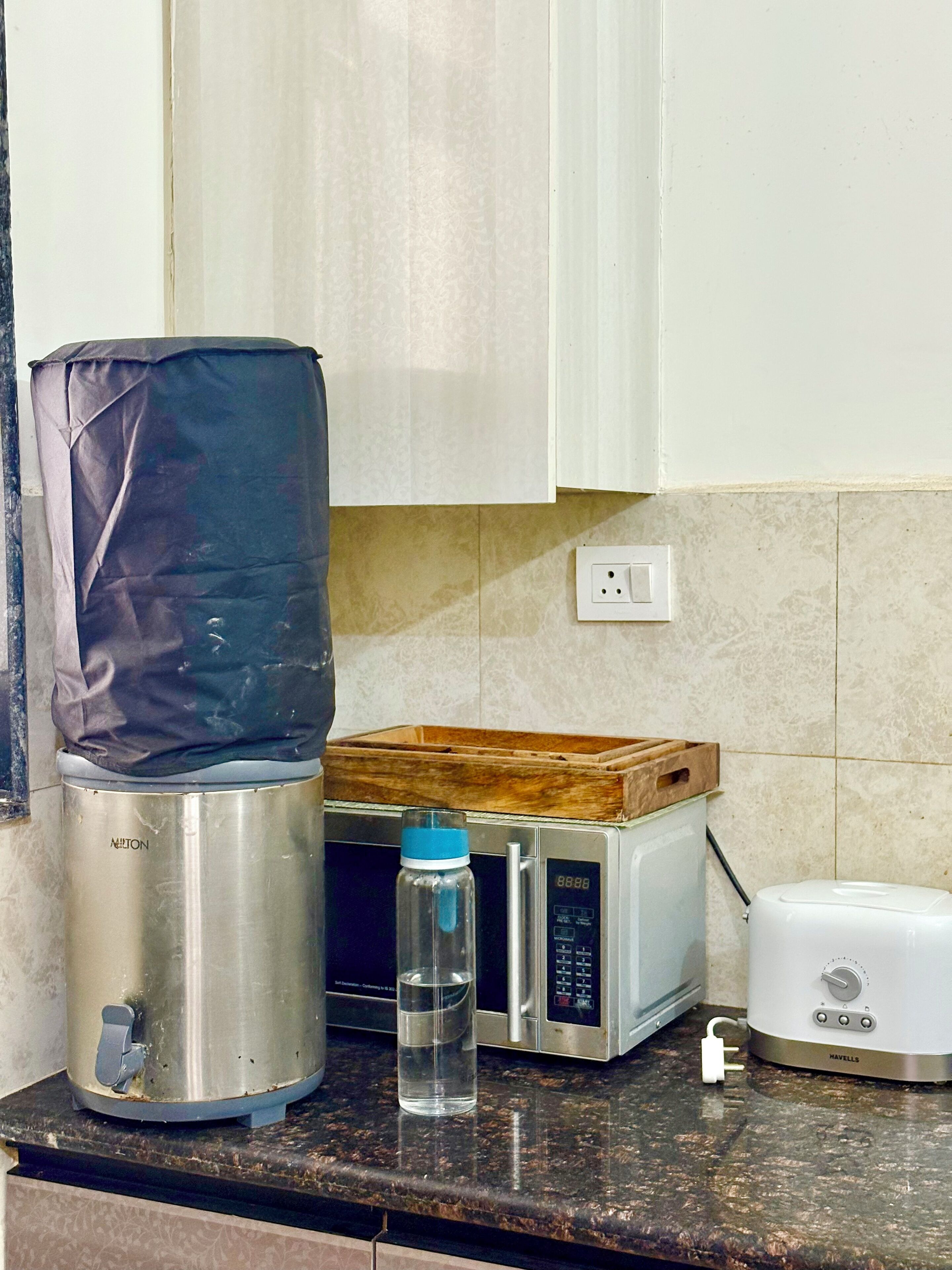 Una cocina con tetera, microondas, tostadora y una botella de agua sobre la encimera.