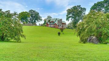 A large, multi-story house with a green roof, surrounded by lush green grass and trees.