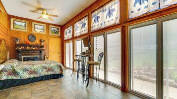 A room with a bed, a fireplace, a table with chairs, and large windows with curtains.