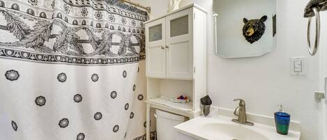 A bathroom with a patterned shower curtain, a white toilet, a sink with a mirror, and a bear head decoration.