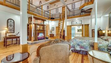 A spacious loft-style room with a high ceiling, wooden beams, a fireplace, a large bed, a chair, and a table.