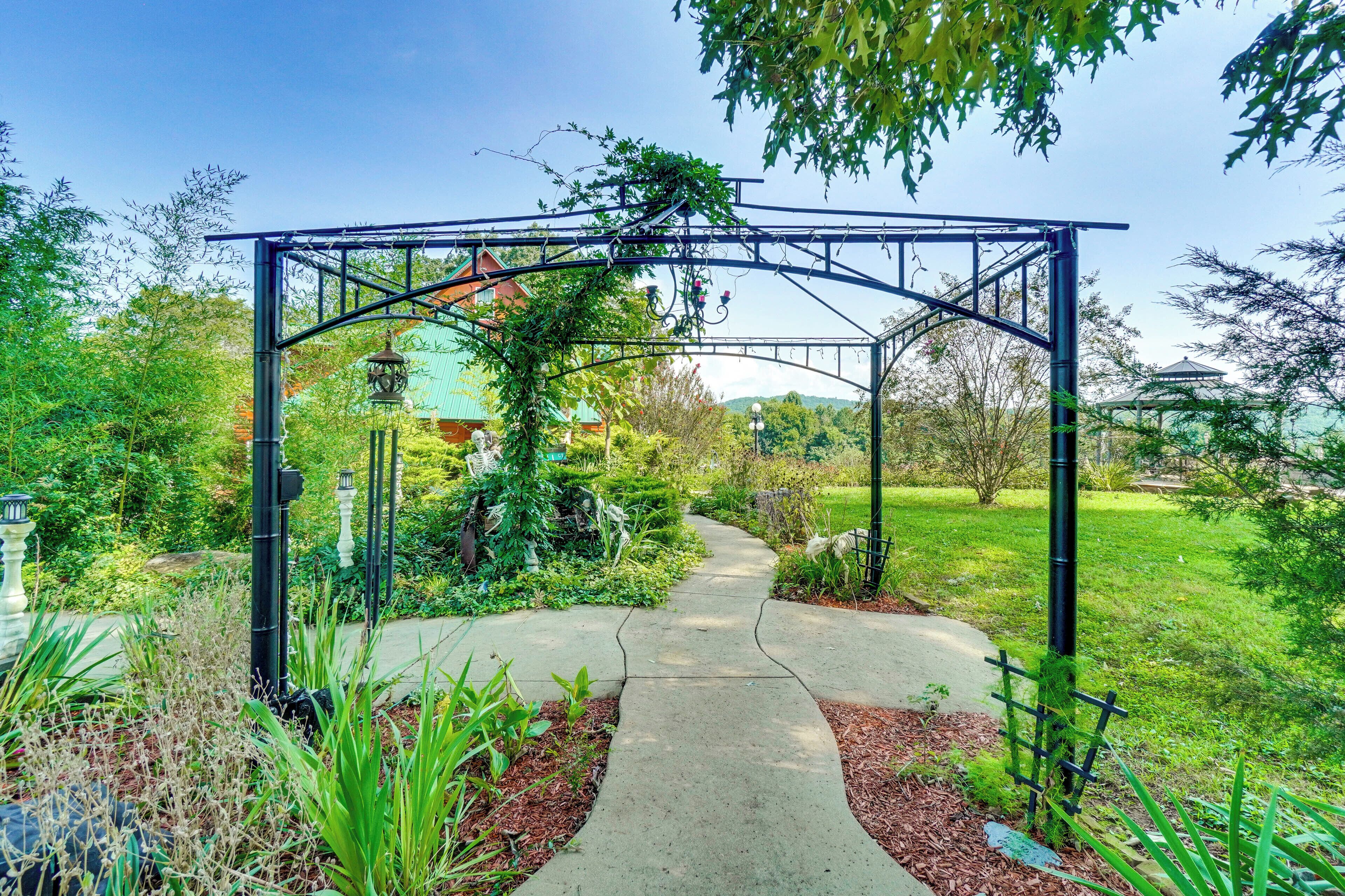 A garden pathway leading to a metal archway with a bench and a lamp post.