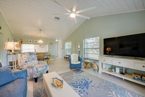 A spacious living room with a ceiling fan, a television, and a dining area with a table and chairs. - Walk to the Gulf Coast! 55+ Retreat w/ Pool Access (Englewood)