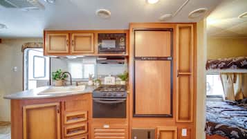 A compact RV kitchen with a stove, sink, and microwave.