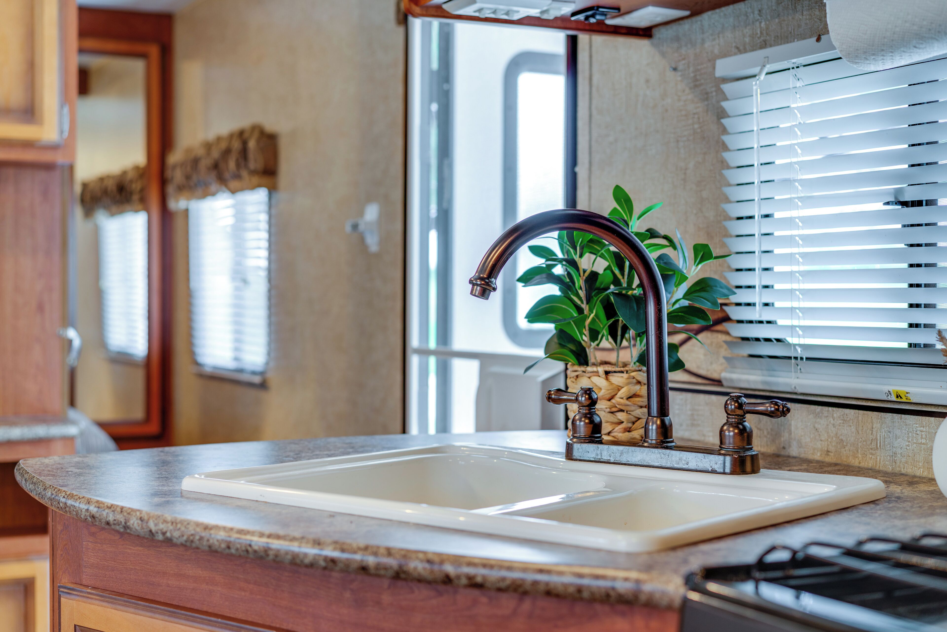 A kitchen with a sink, a window with blinds, and a potted plant.