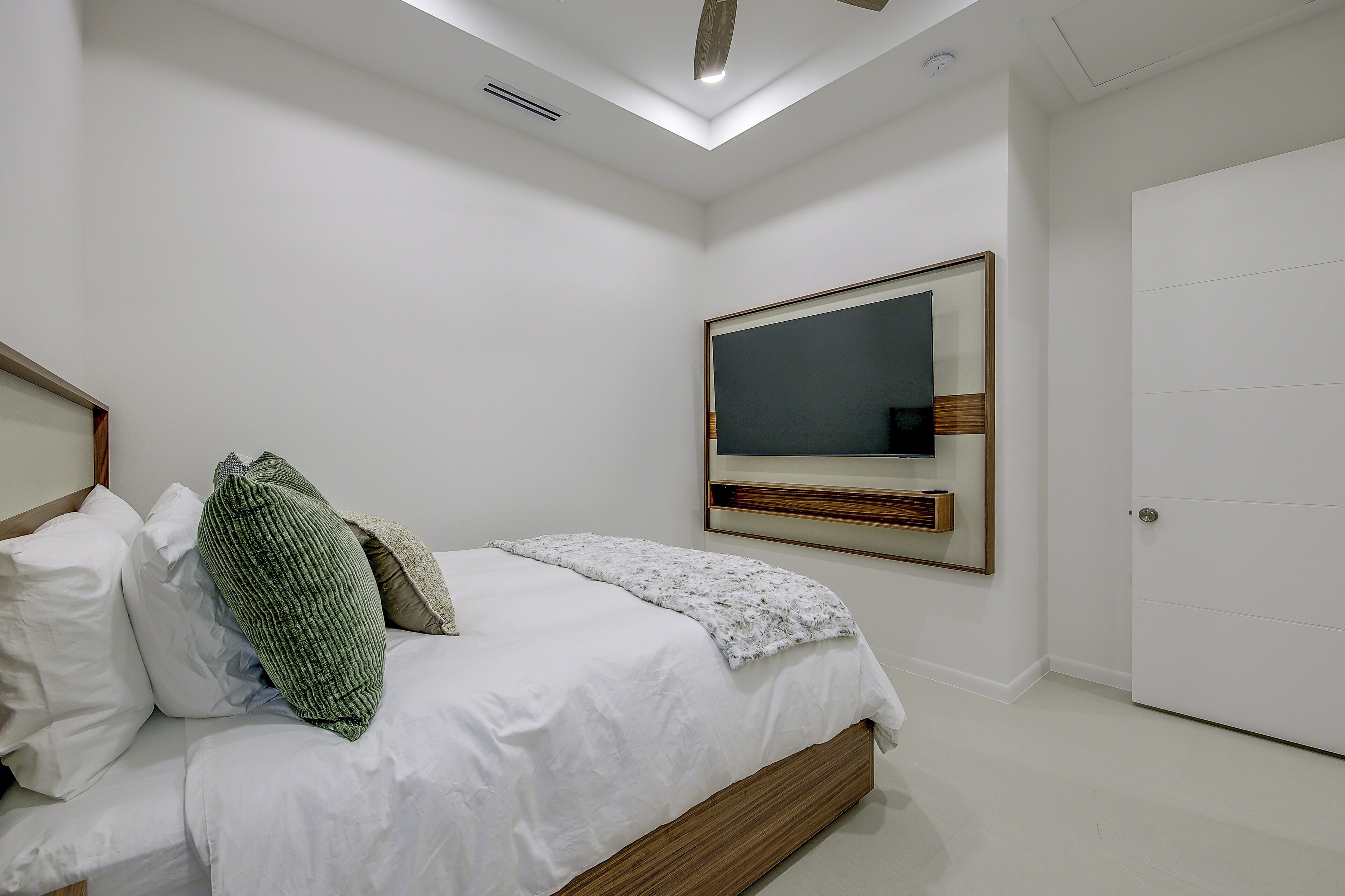 A bedroom with a bed, pillows, a bedside table, a mirror, and a door.