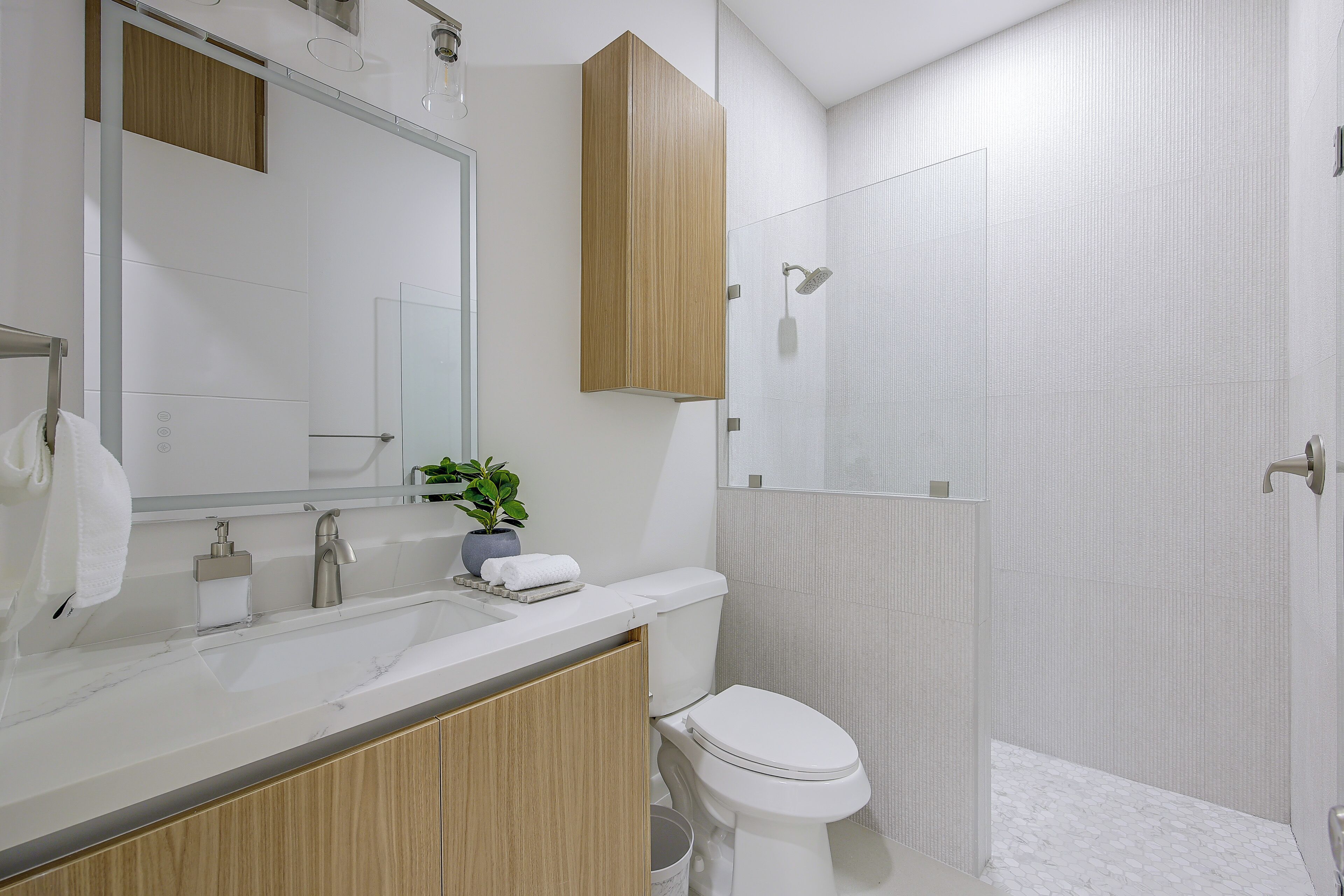 A modern bathroom with a white sink, a mirror, a wooden vanity, a toilet, and a shower enclosure.
