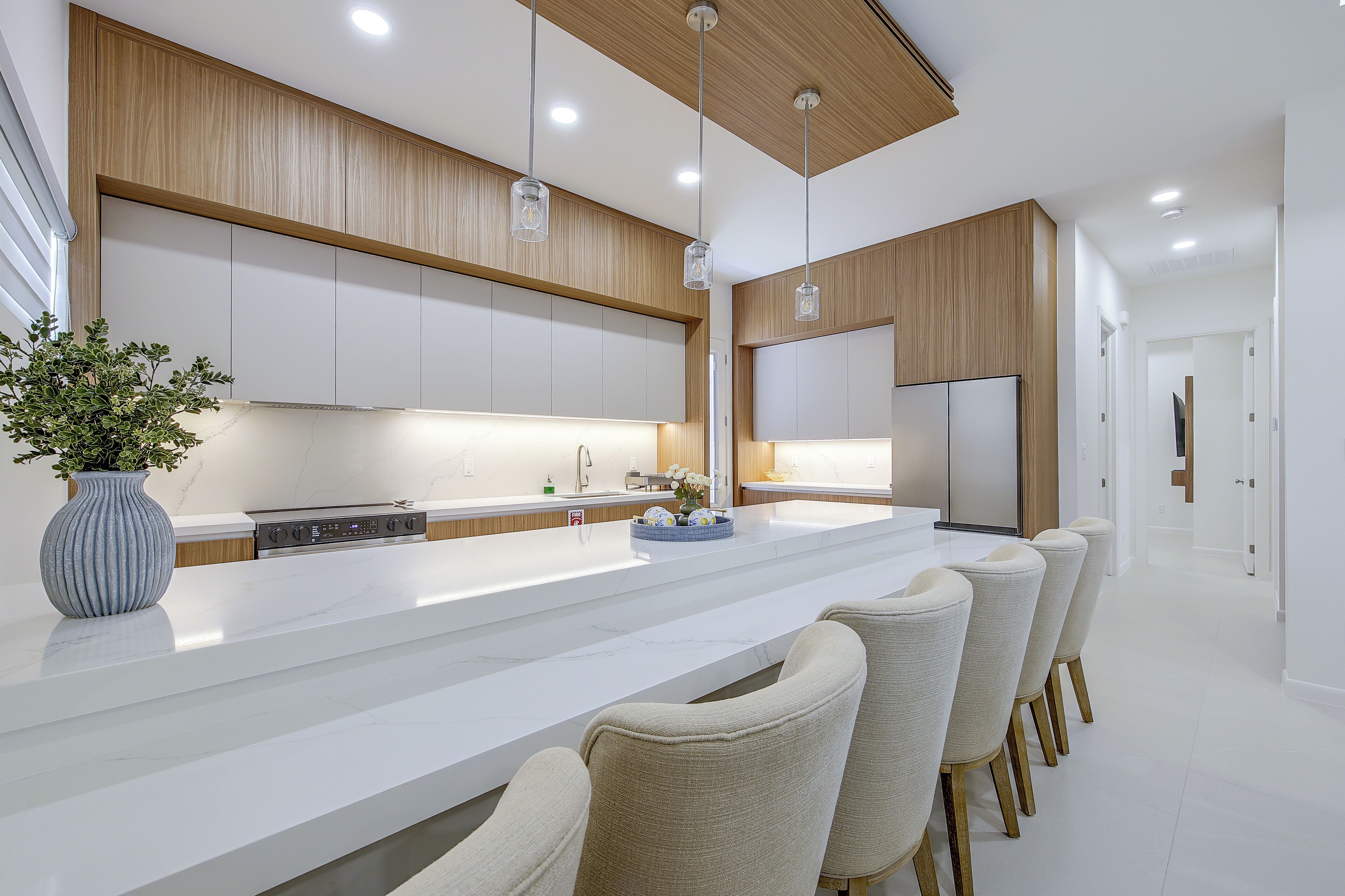 A modern kitchen with a large island, bar stools, pendant lighting, and a built-in oven.
