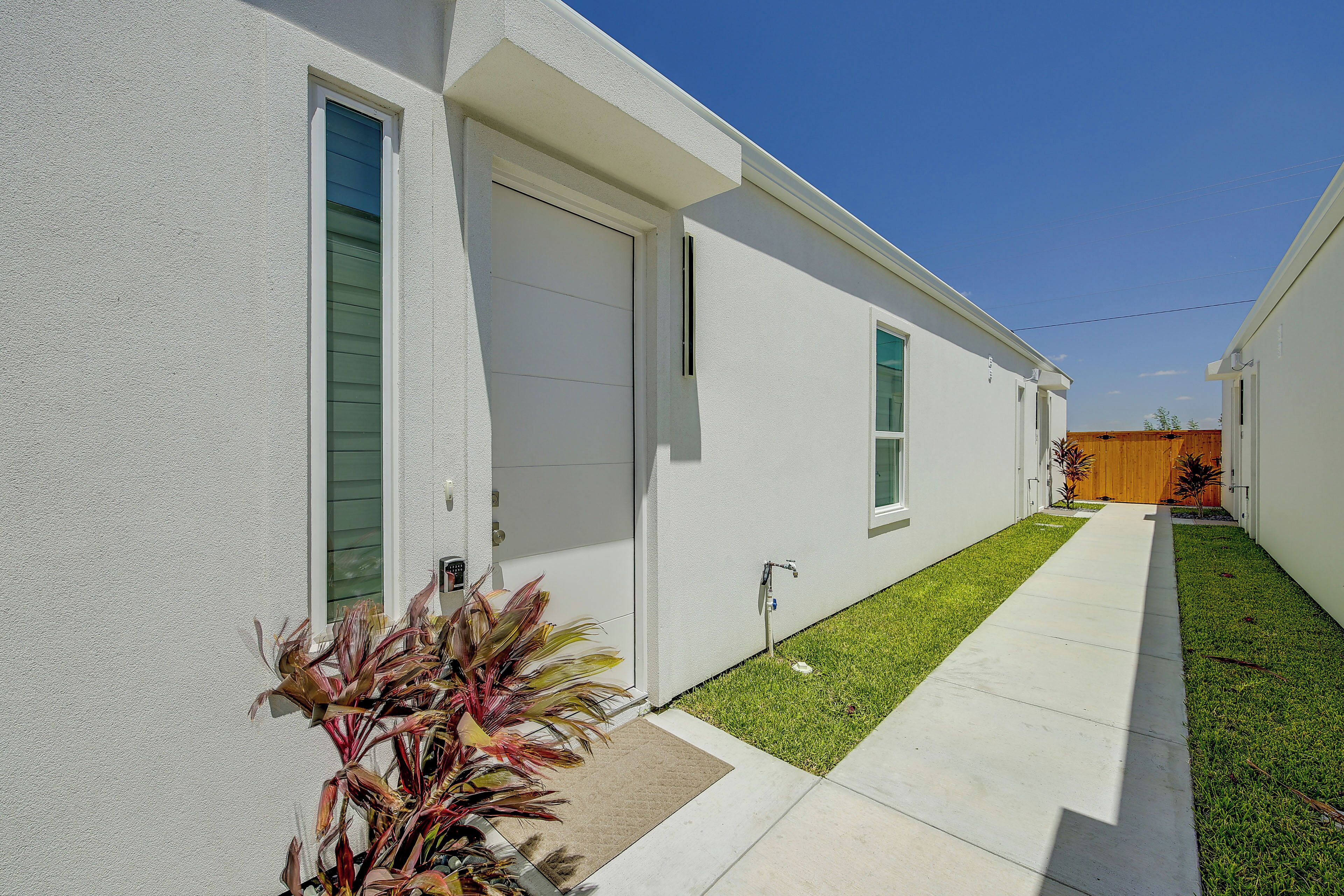 A modern two-story residential building with a clean facade, a small front yard, and a clear sky.