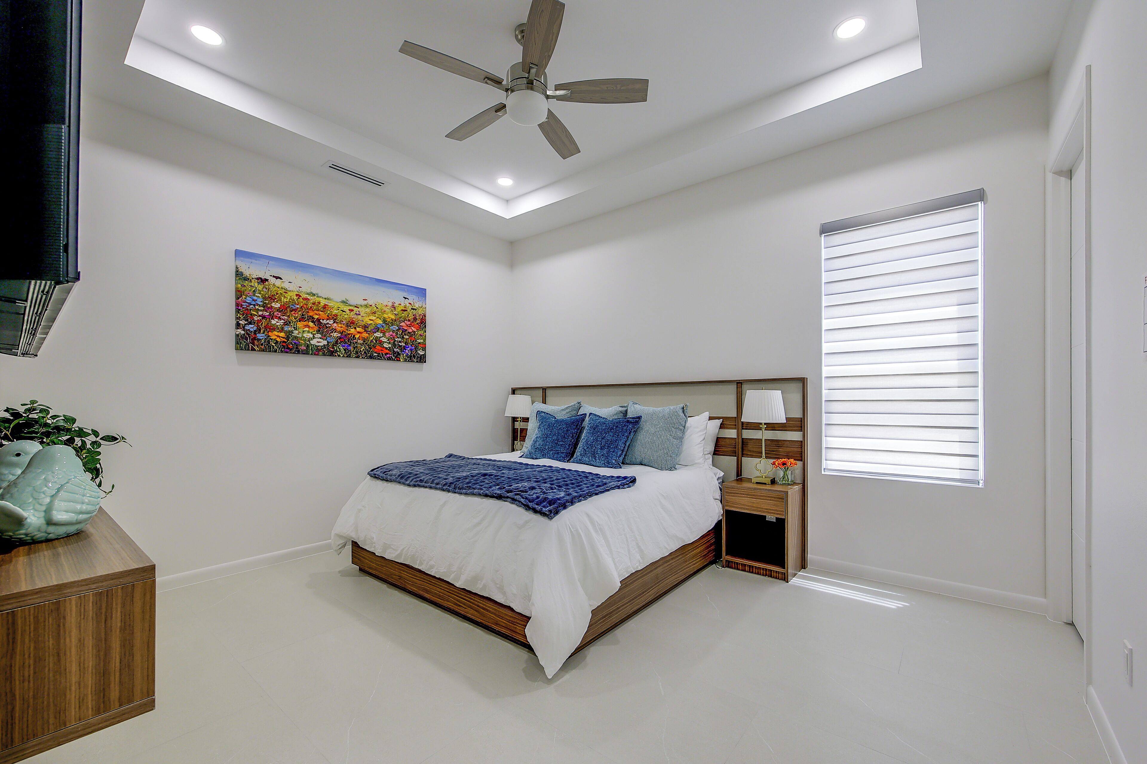 Quarto com cama, ventilador de teto, pintura e janela com persianas.