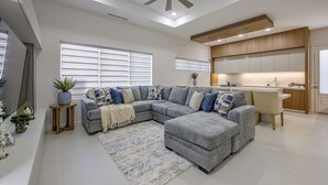 Una sala moderna con un sofá modular, un ventilador de techo y una zona de cocina con armarios de madera.