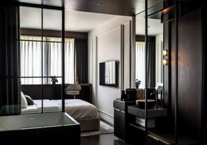 A modern hotel room with a bed, a desk, a vanity with a mirror, and a large window with curtains.