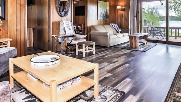 A wooden-paneled living room with a sofa, coffee table, and artwork. - Welcome to Sunset Cove, in the center of Wisconsin's scenic Northwoods. (St.Germain)