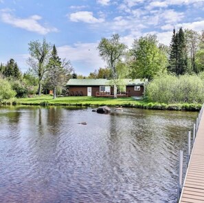 A lakeside property with a wooden dock, a house with a green roof, and a pond.