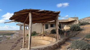 Una casa con un camino de piedra que lleva a un espacio exterior cubierto, una piscina y vistas del paisaje circundante.