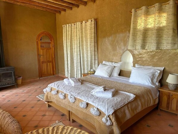 Un dormitorio con cama, cortinas, una puerta de madera, una mesita de noche y una lámpara.
