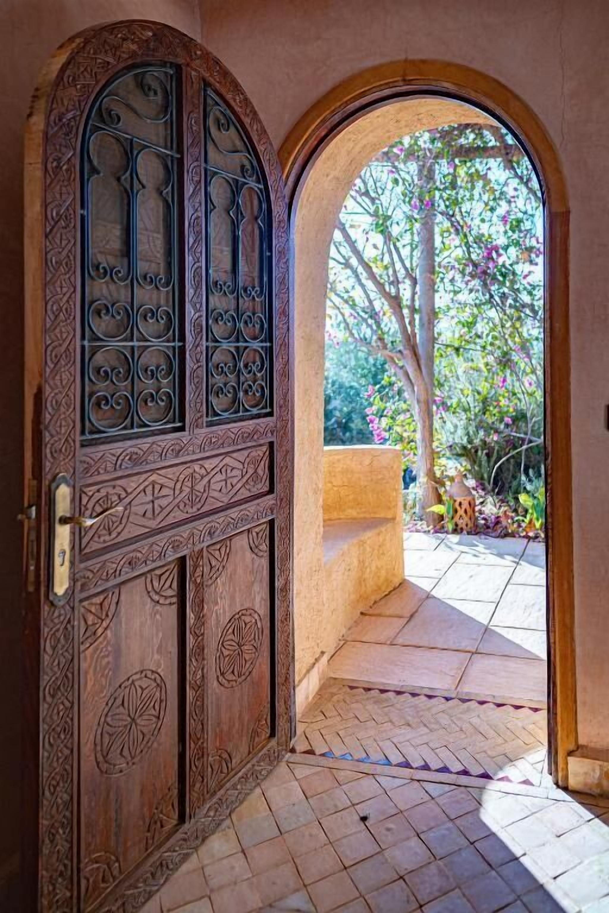 Un arco di ingresso che conduce a un cortile con pavimento piastrellato e un albero con fiori rosa.