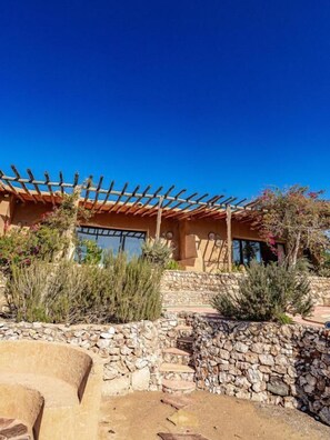 Un muro de piedra, una pérgola de madera y un edificio con amplios ventanales.