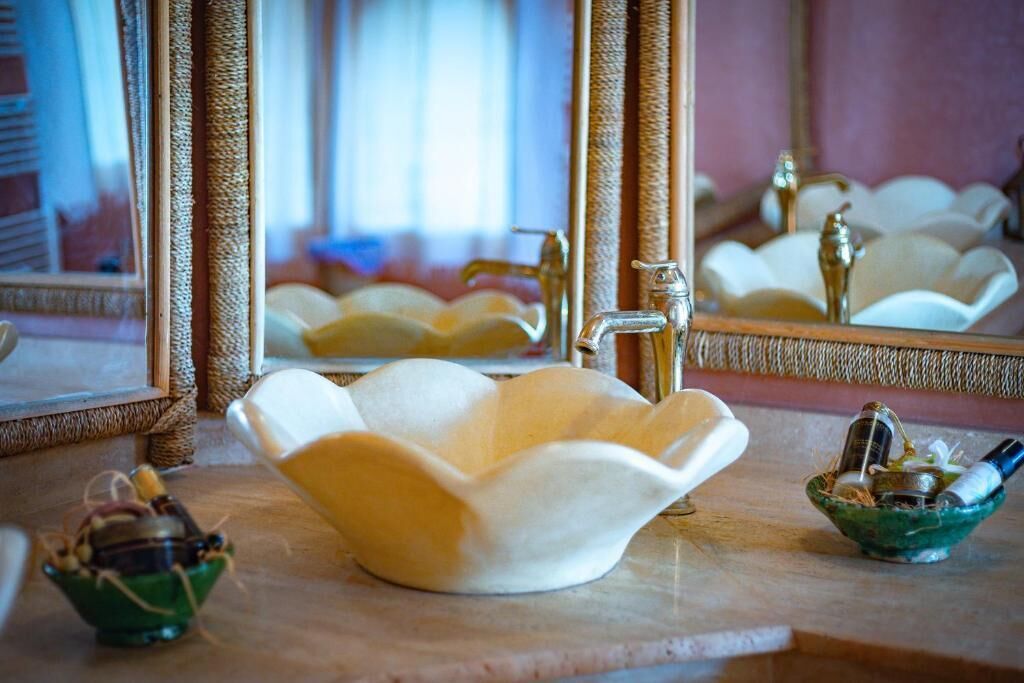 Un baño con un lavabo blanco con forma de flor, un espejo y dos recipientes pequeños sobre la encimera.