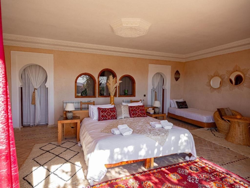 A bedroom with a large bed, two bedside tables, a nightstand, a small sofa, and a window with curtains.