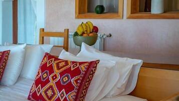 A hotel room with a bed, a wooden nightstand, a bowl of fruit, and a window with an arched frame.