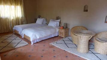 A bedroom with two beds, a nightstand, wicker furniture, and a tiled floor.