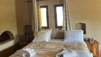 Un letto matrimoniale con una coperta a motivi decorativi e due cuscini, un comodino con una lampada e una finestra con tende.