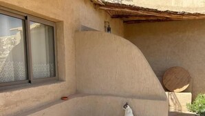 Un banco de hormigón curvo con un perro pequeño sentado encima, una mesa de madera redonda y una ventana con vistas.