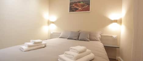 Une chambre d’hôtel avec un grand lit, deux lampes fixées au mur et un tableau accroché au mur.